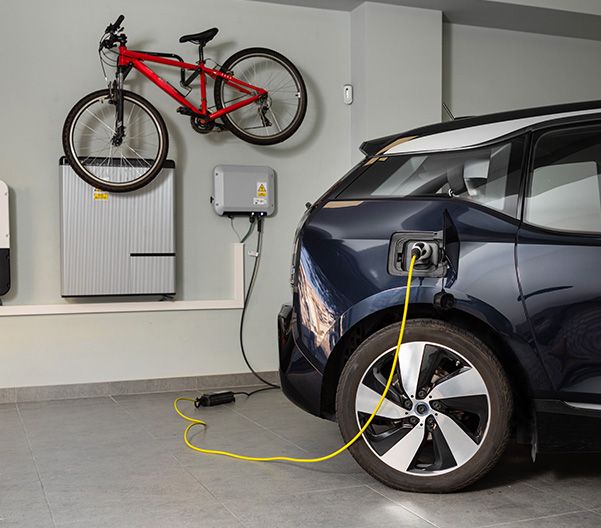 En elbil laddas via en laddbox i ett garage med en röd mountainbike på väggen.