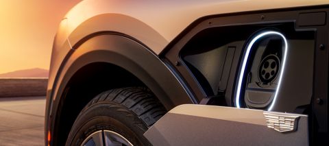 Närbild på en elbil med öppen laddlucka i solnedgång.